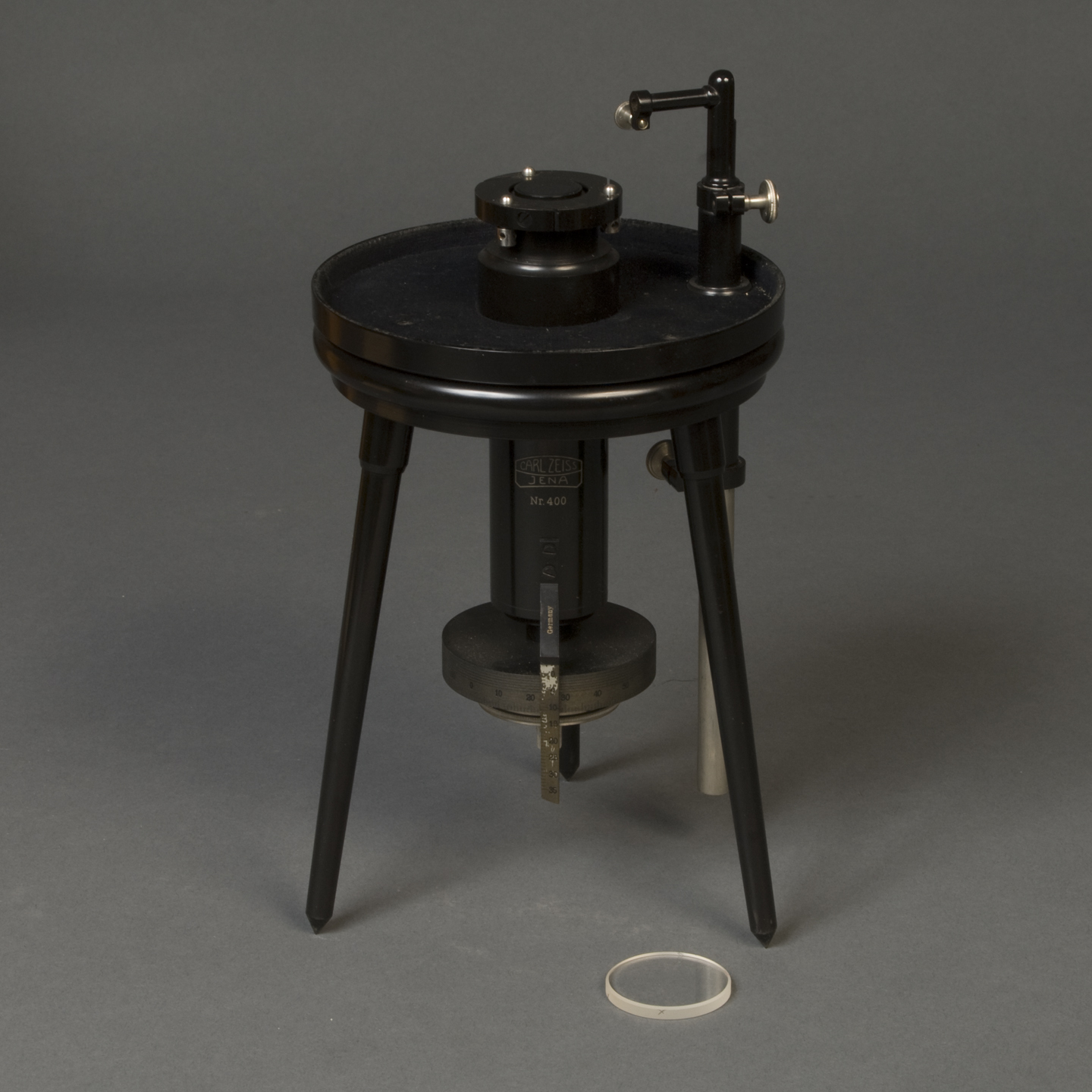 tripod device with lens. The words "Carl Zeiss, Jena, Nr. 400" appear on a cylinder that extends below the tripod's platform. Below that is a graduated dial, presumably for raising and lowering the platform. 