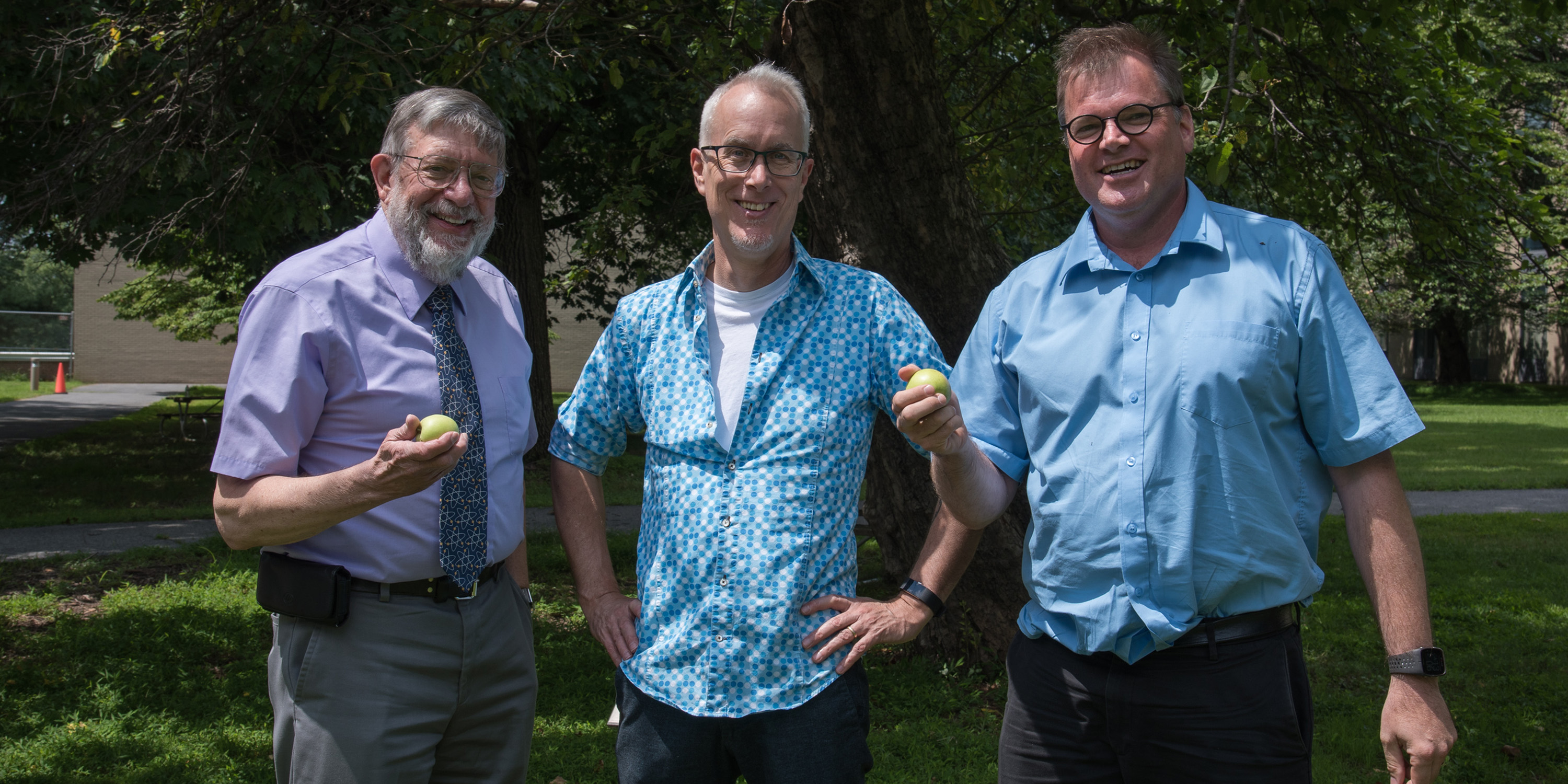 Bill Phillips, Jon Pratt and Stephan Schlamminger smile before the Newton apple tree on the NIST Gaithersburg campus. Bill and Stephan are holding small apples from the tree.