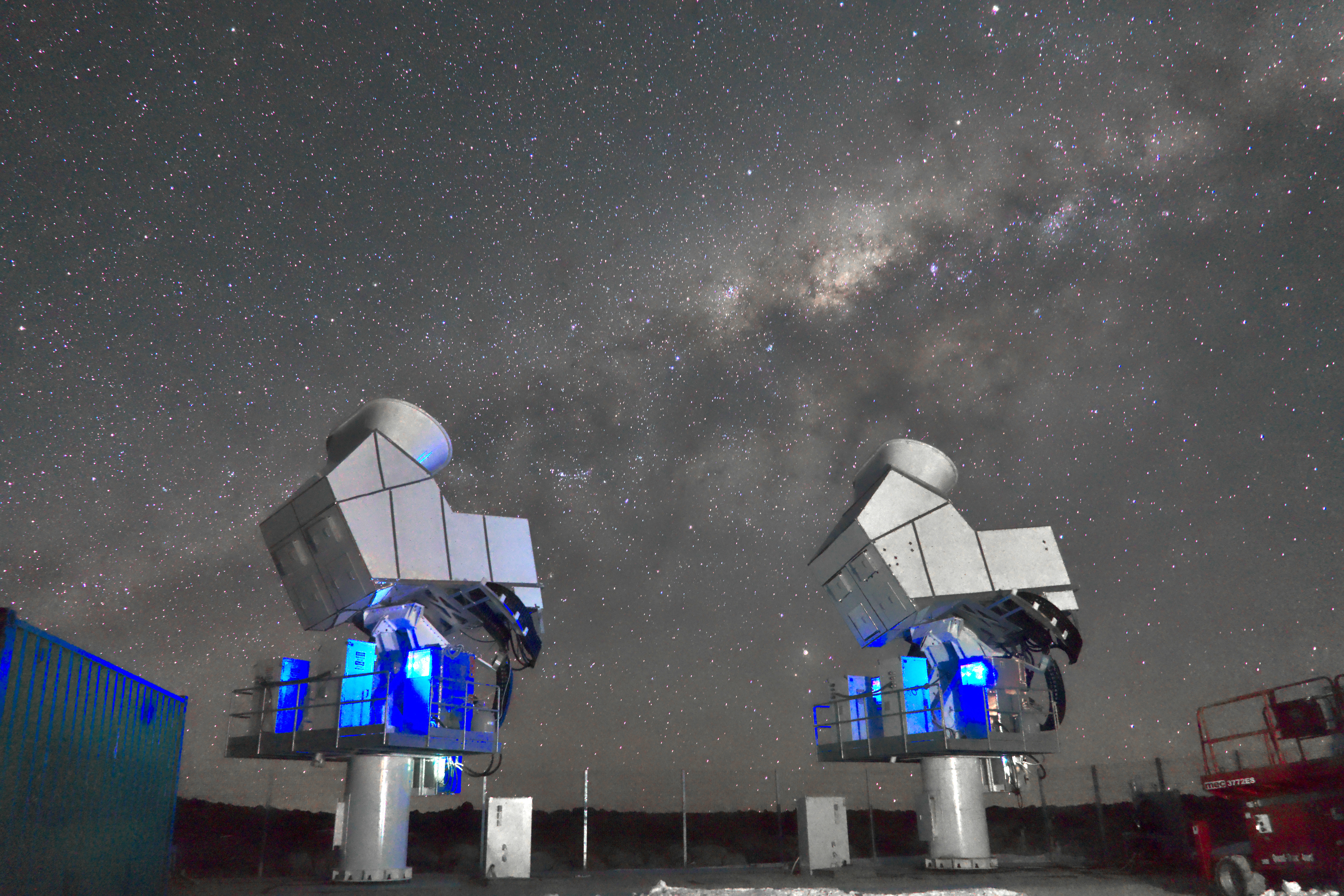 Two telescope structures stand in front of a starry night sky. 