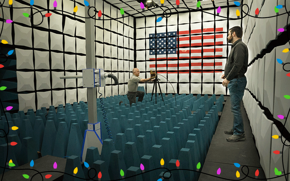 Two men prepare equipment in a room with gridlike walls of white boxes. Blue cone-shaped objects line the floor. An American flag is painted on the back wall.