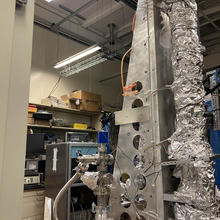 Large scientific device in lab has tall cylindrical portion wrapped in aluminum foil.