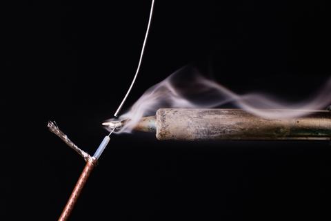 Photograph of smoldering soldering iron melting solder onto an electrical cable. 
