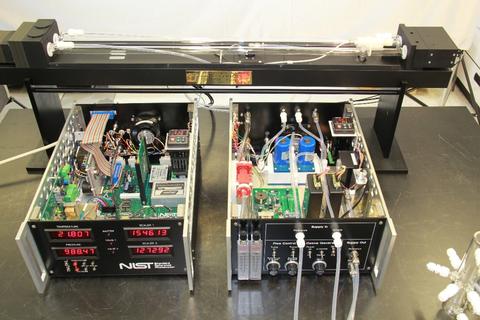 Photograph of the NIST Standard Reference Photometer showing the component modules consisting of optical bench with sample and reference tubes, ozone generator module with controls and tubing, and control module with numeric LED displays. 