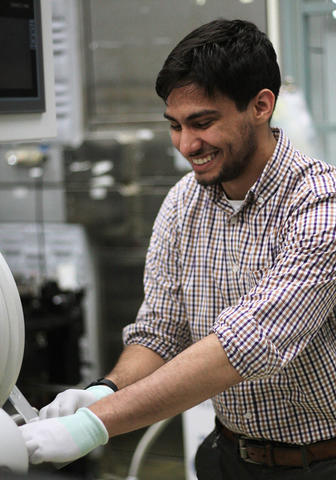 Samuel Márquez González grins as he stands in the lab handling scientific equipment. 