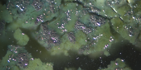 Close-up shows shiny metal patches with areas of green corrosion and open holes. 