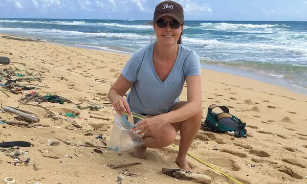 woman kneeling on a Hawaiian beach putting plastic trash into a bag