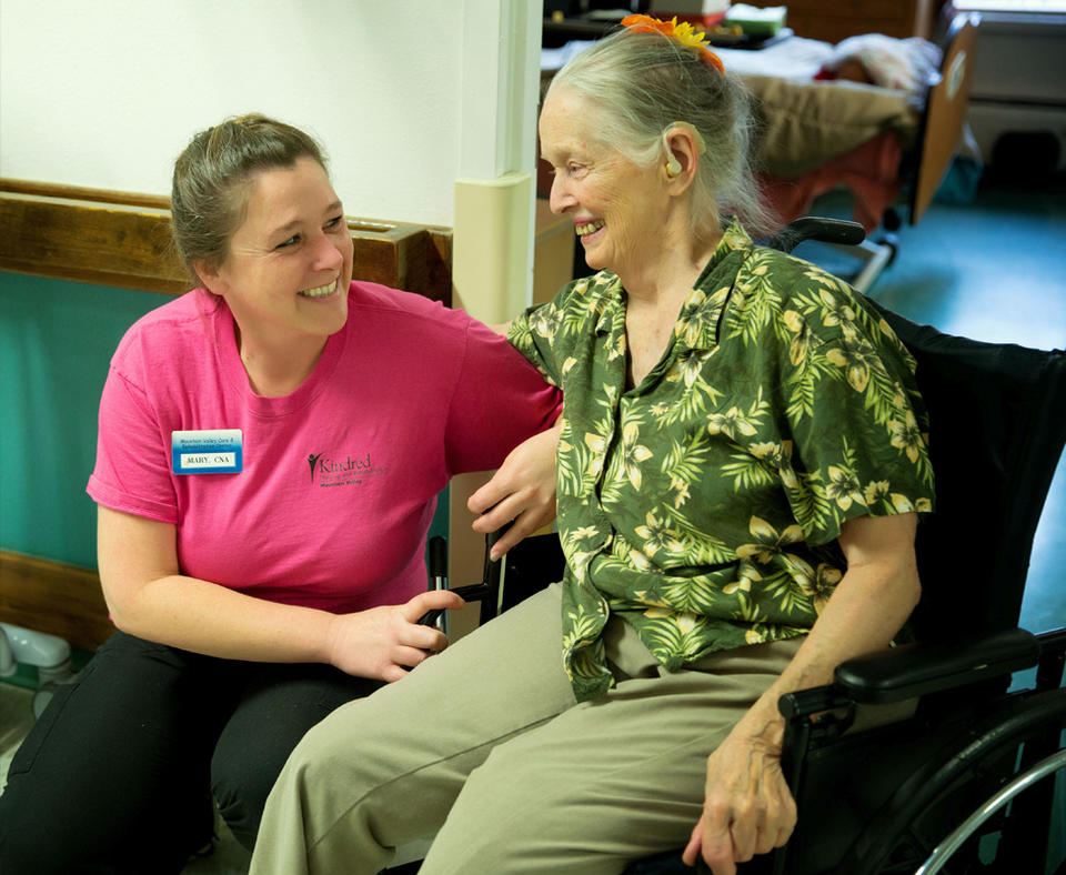 Photo of Kindred Nursing and Rehabilitation Center – Mountain Valley employee helping a patient in a wheelchair.