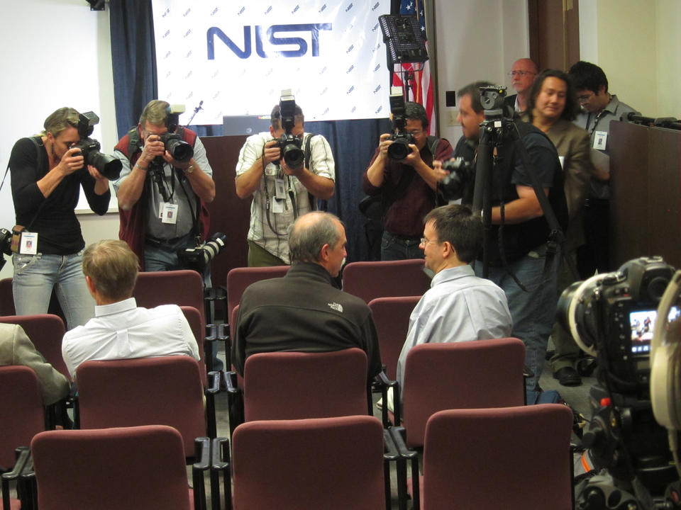 Dave Wineland (left) and Eric Cornell (right) sitting in chairs while photographers take their picture