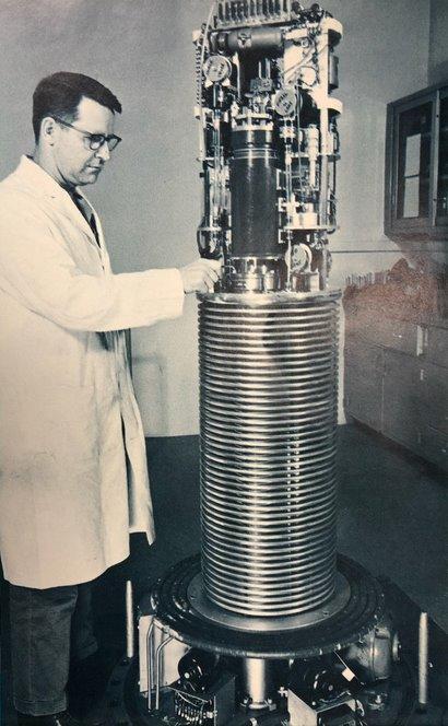 A man in a lab coat stands to the left of a tall piece of equipment