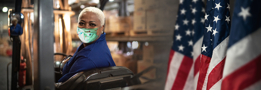 Portrait of female worker driving forklift in warehouse in a face mask