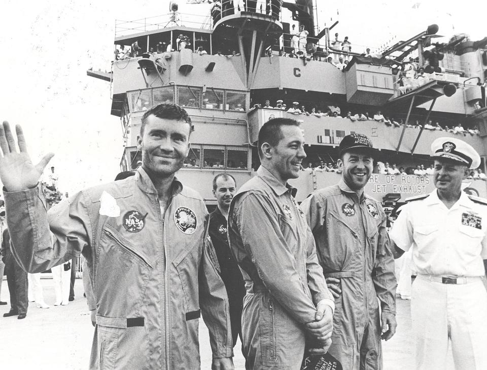 Historical photo shows three returned Apollo 13 astronauts posing for a photo op with an aircraft carrier in the background crowded with well-wishers.