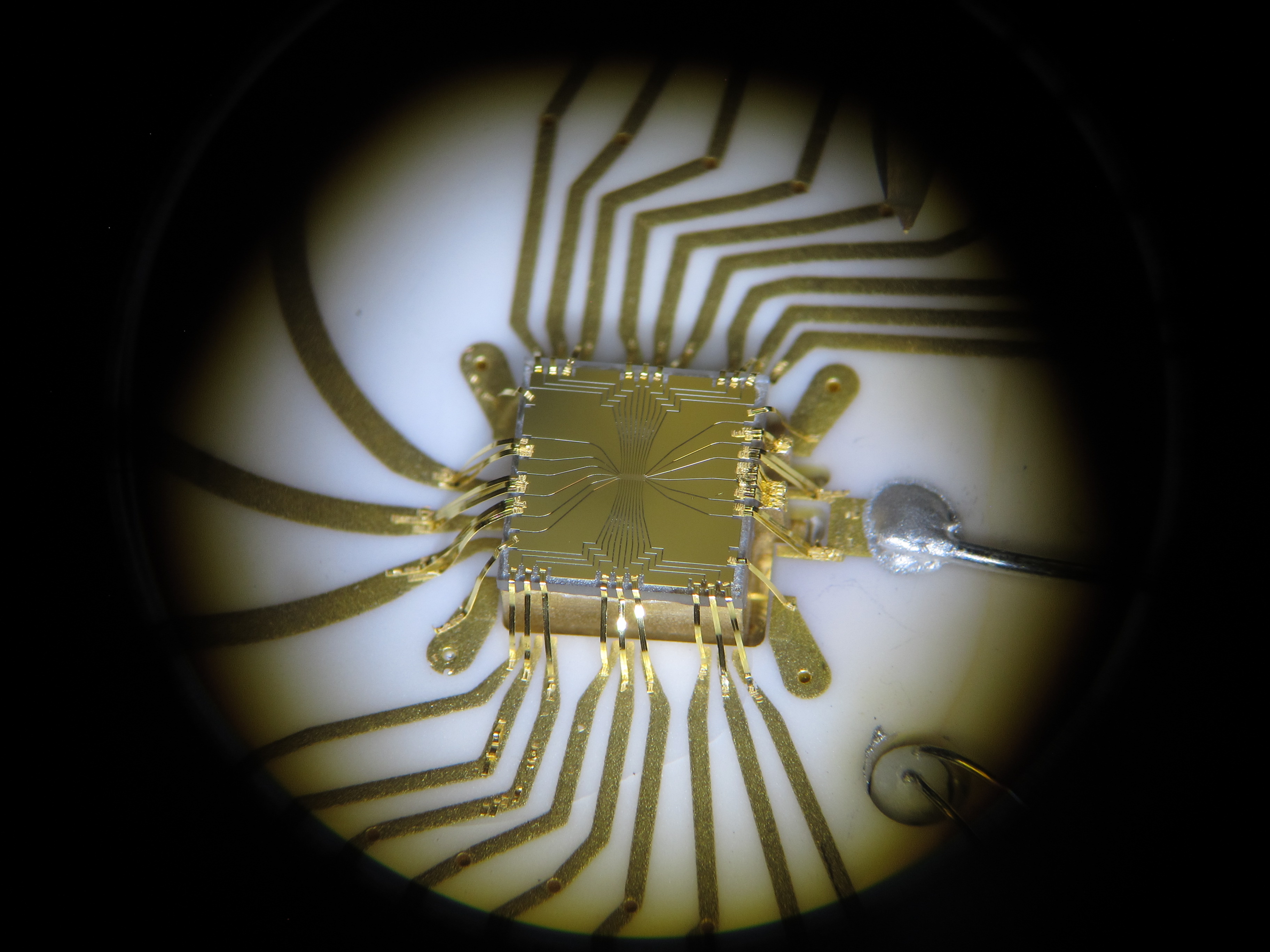 close-up of an ion trap, a small square golden box with electronic leads running to it and circuits engraved into it 