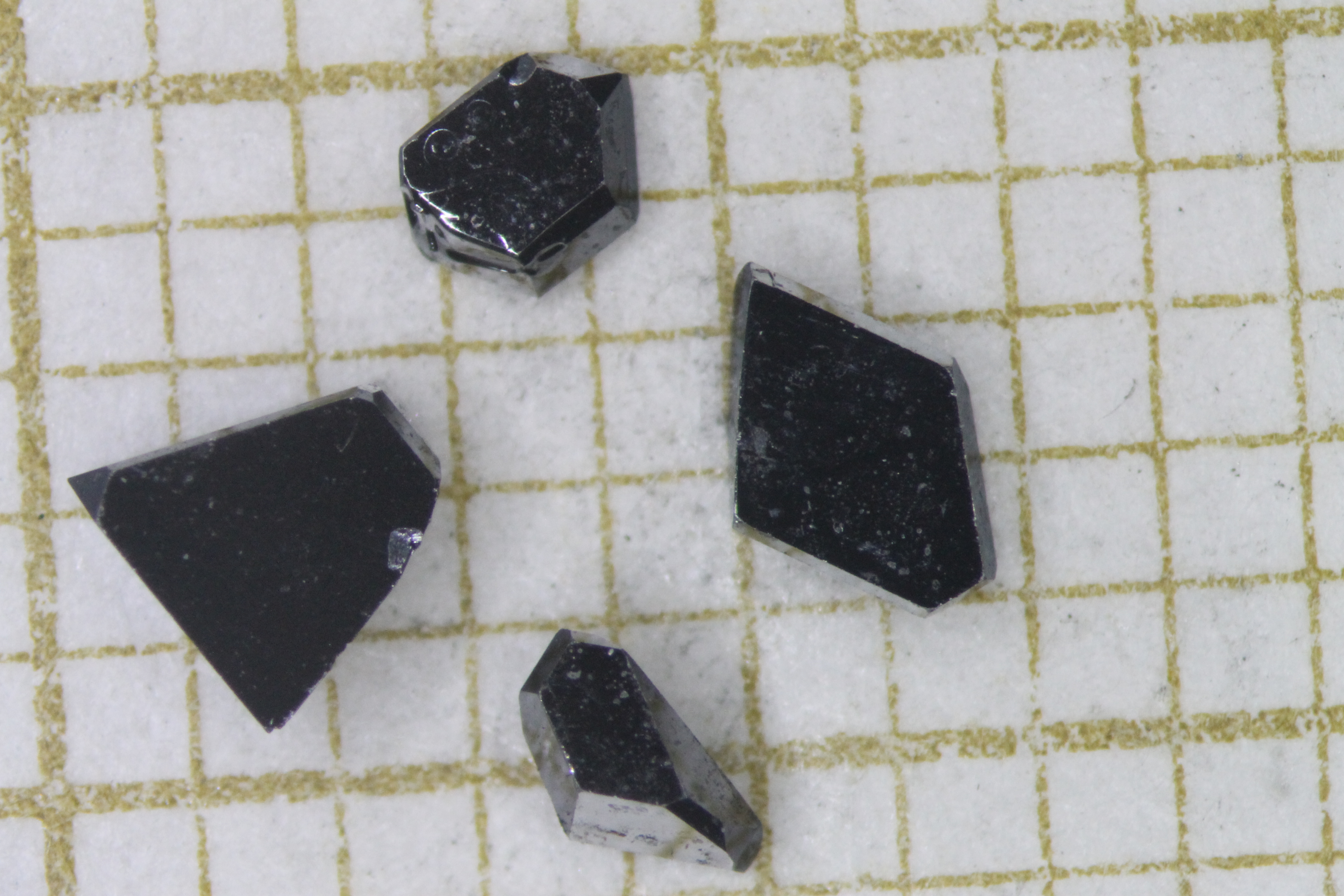 close up of four differently sized shiny black crystals of uranium ditelluride on a sheet of graph paper