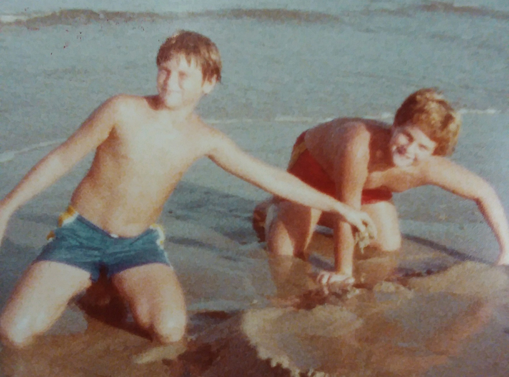 two smiling young boys playing in the sand at the beach