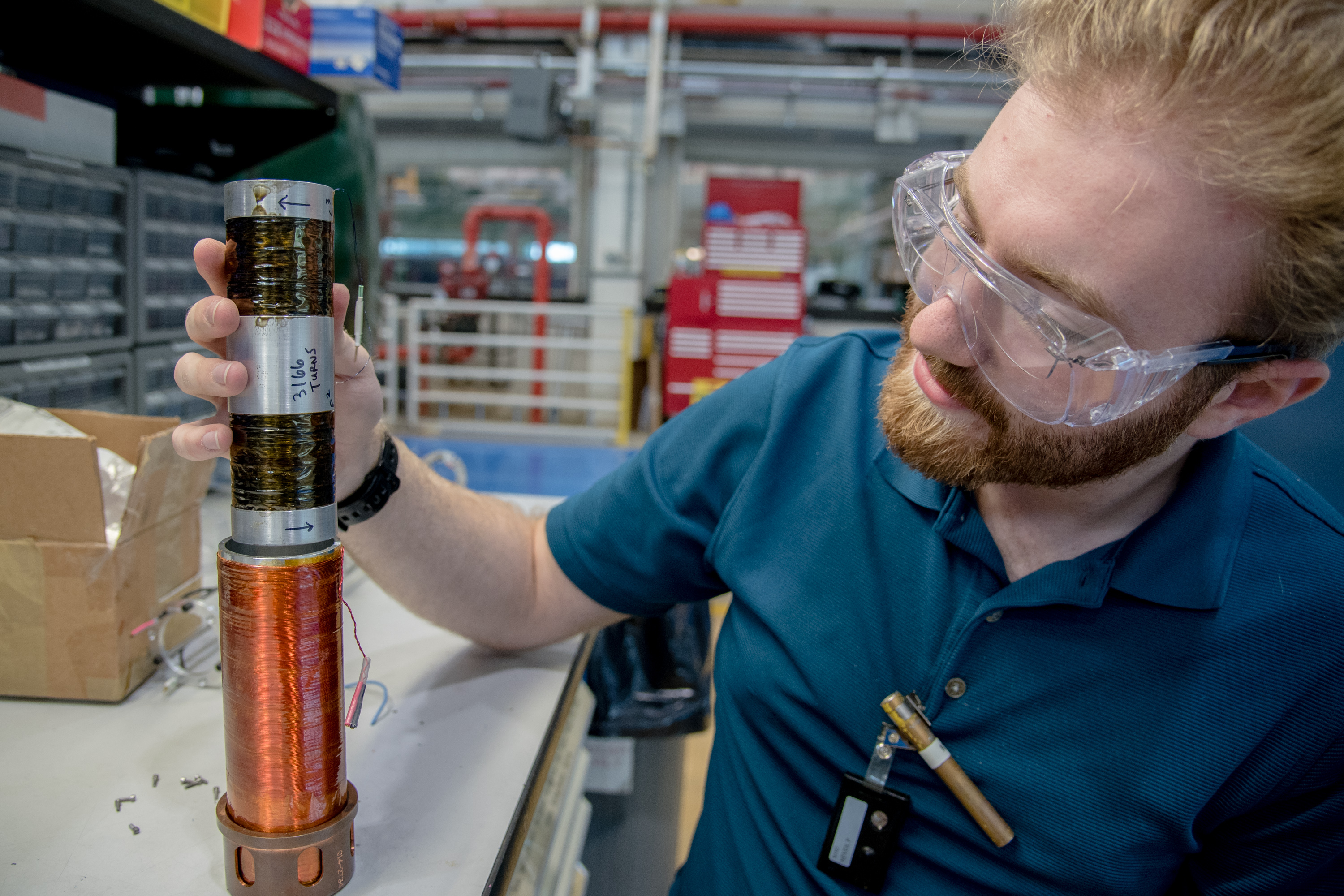 Paul inspects a short metal rod with coils of wire wrapped around each end. 