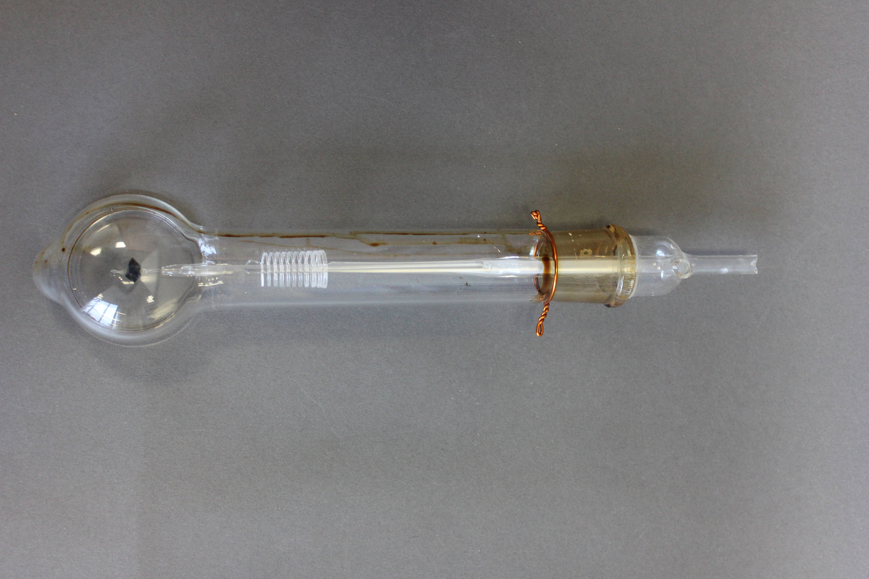 a glass tube with a bulb at one end. there is a glass filament running through the center of the tube that coils on the bulbous end. there is a brass-colored plug at the other end where the tube tapers to a smaller straight tube