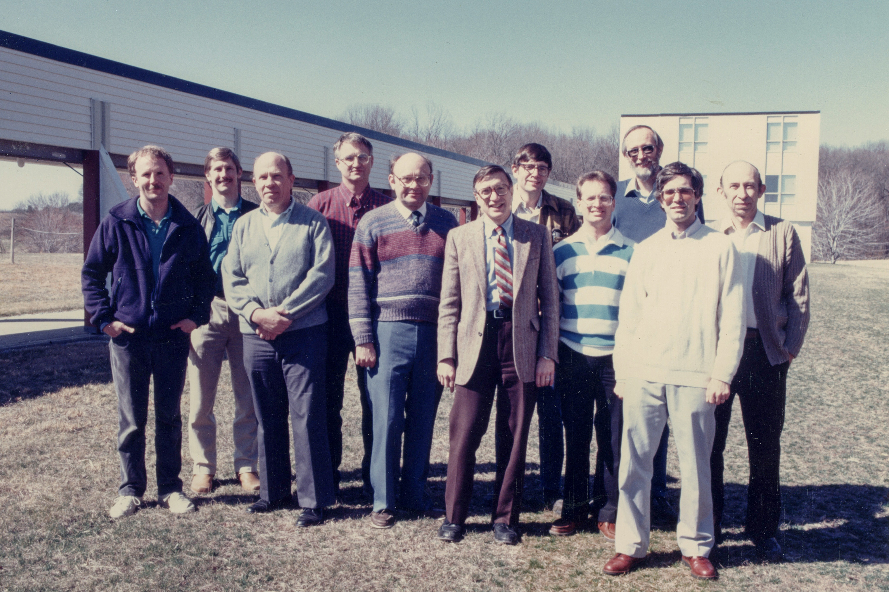 A group of men standing in a grassy field in front of a laboratory