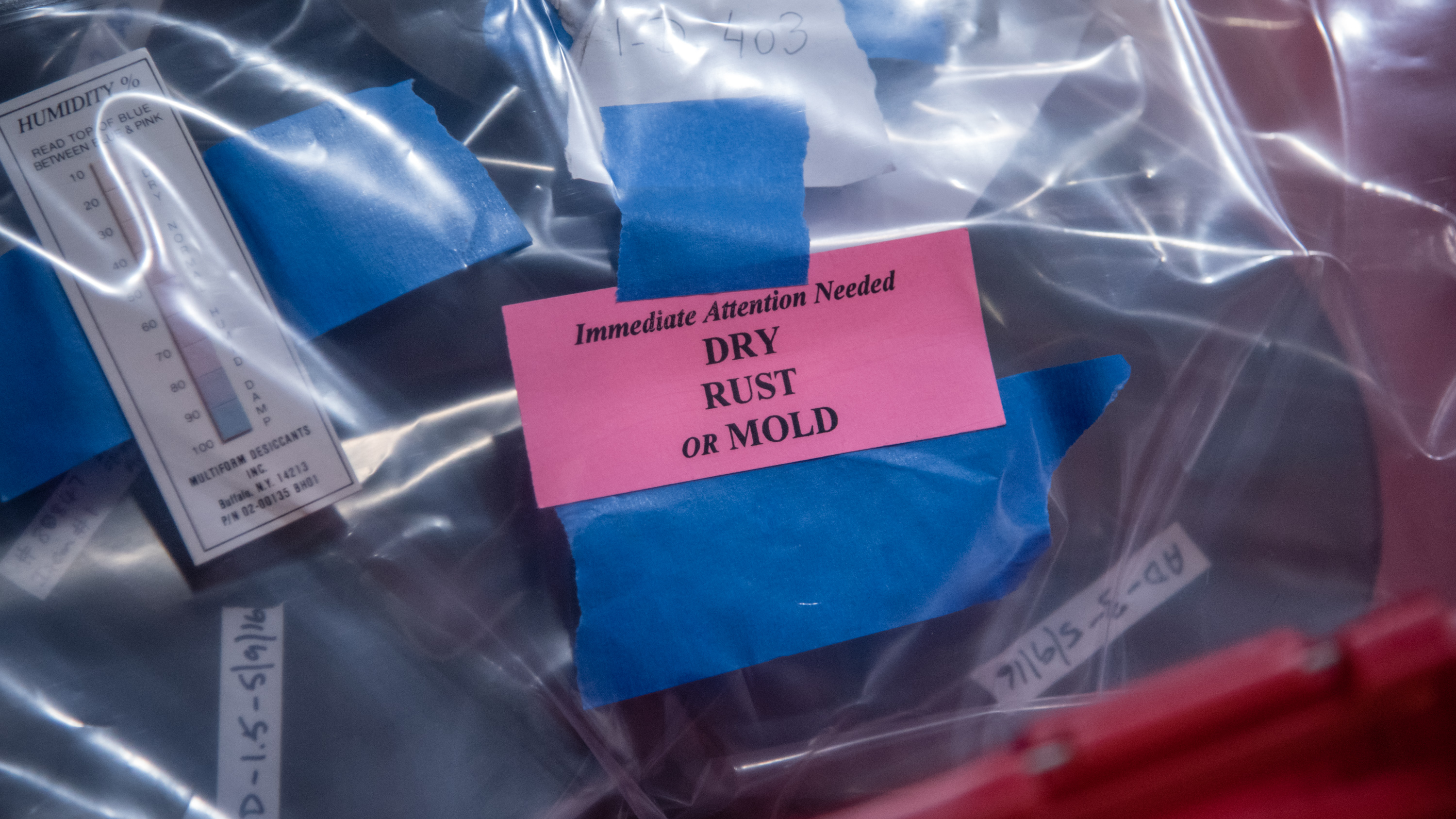 plastic bags containing various objects, a card affixed with blue tape reads "immediate attention needed, dry, rust or mold"