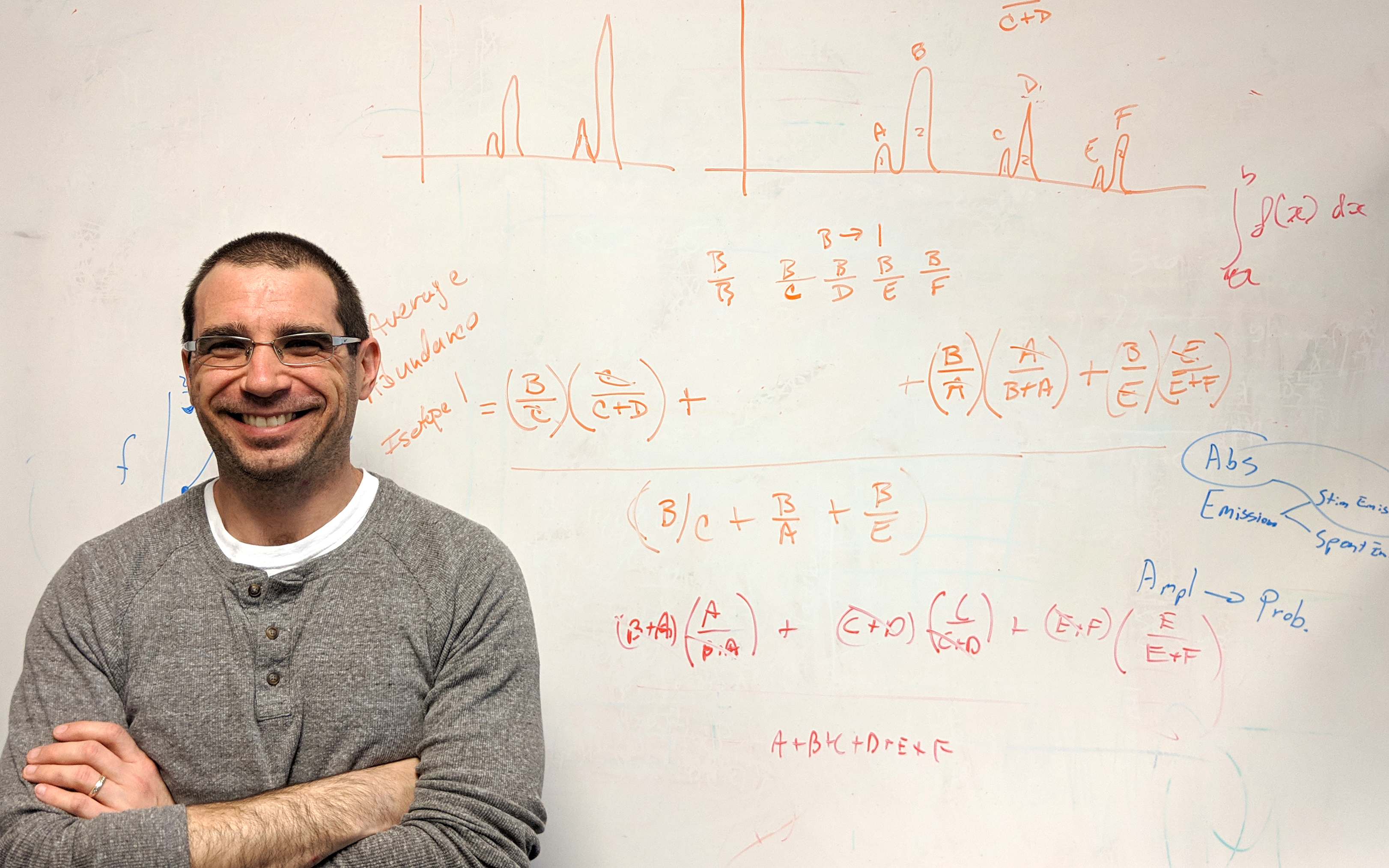 Adam Pintar standing with arms crossed in front of a whiteboard covered with equations and graphs