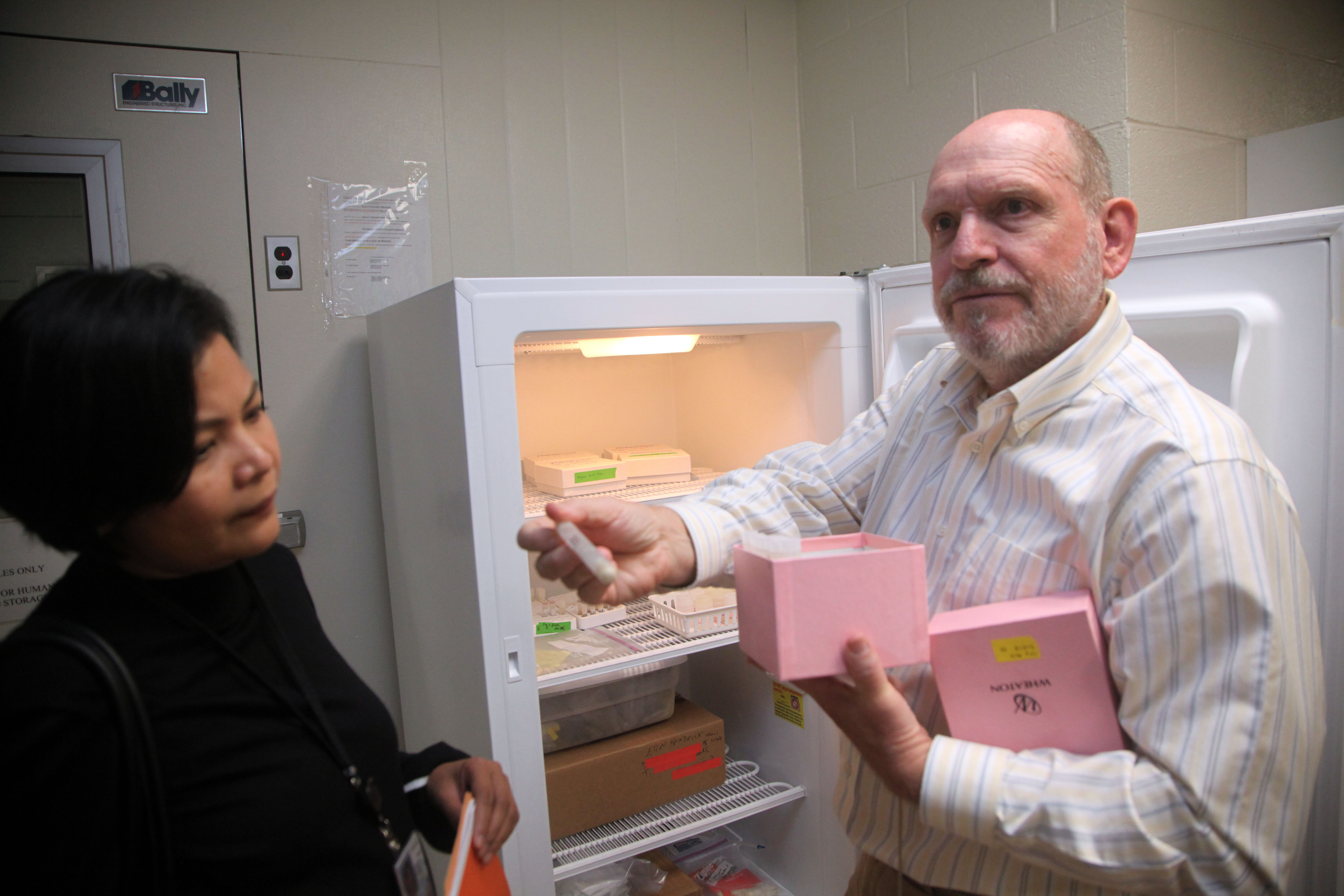 A man and a woman stand outside a freezer. The man is holding out a milk sample in a tube.
