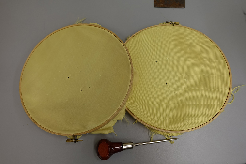 Two round discs. Right one has four holes made with an awl. Left one has two holes.