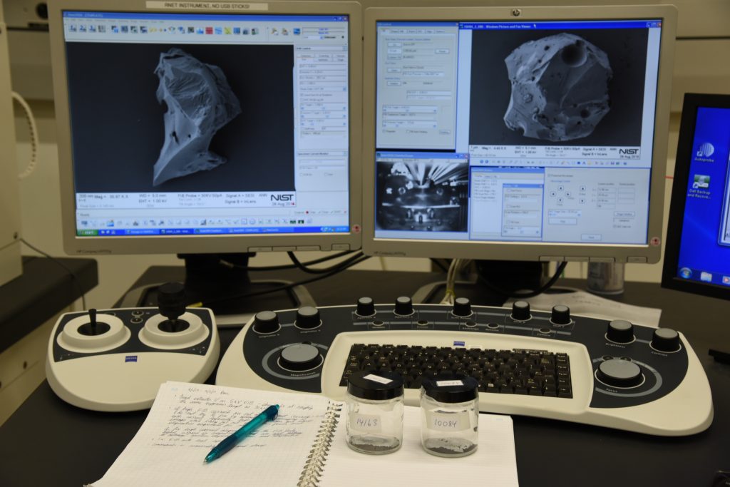 Two monitors. In front: lab notebook with the two moon dust vials