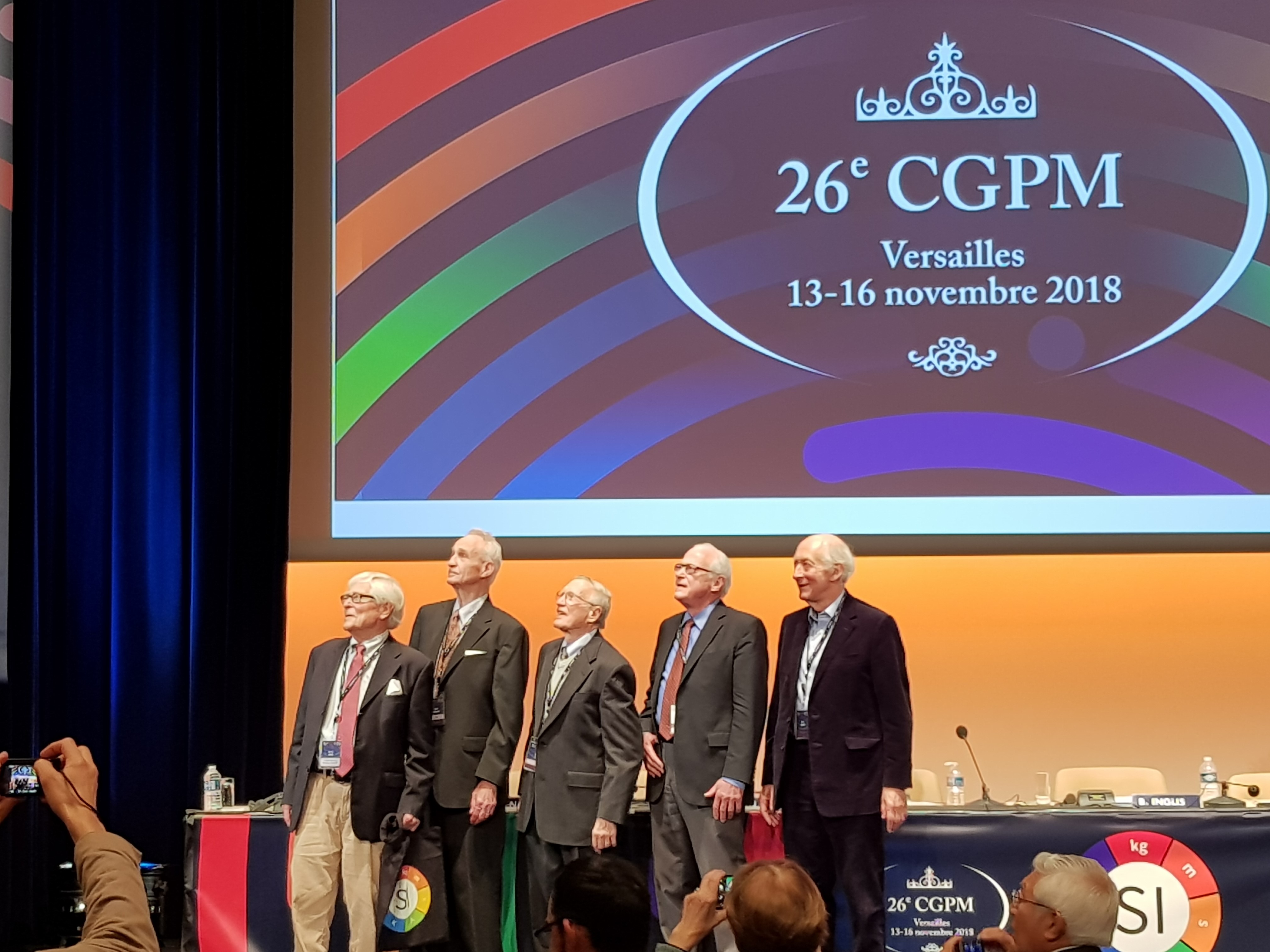 five men standing on a stage looking up and to the left