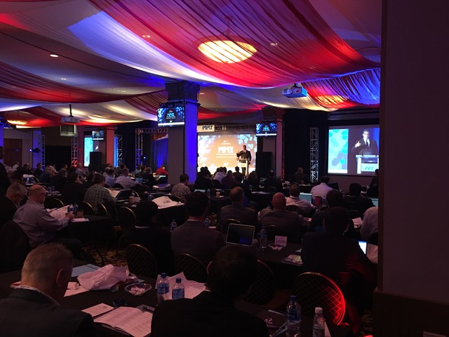 people sitting and watching a speaker present at the front of a room