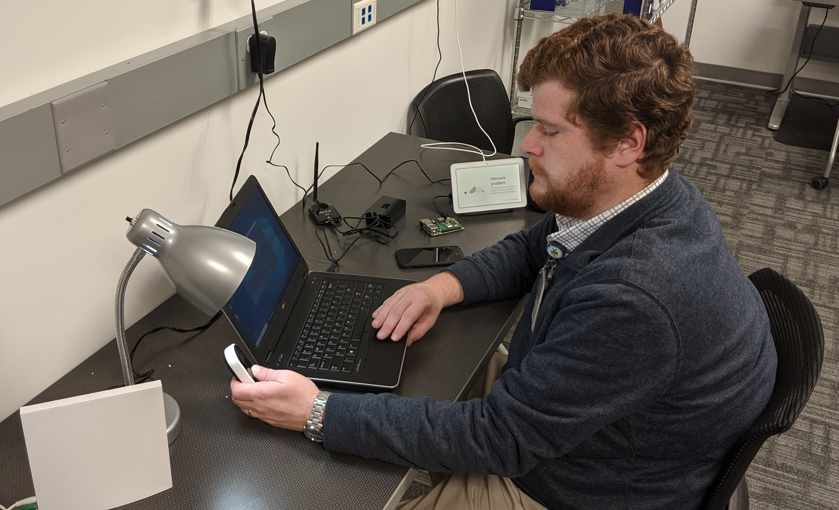 man sitting at a desk with a laptop computer surrounded by various IoT devices