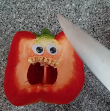 A picture of a halved red pepper with googly eyes attached, and a sharp knife. The pepper looks scared. 