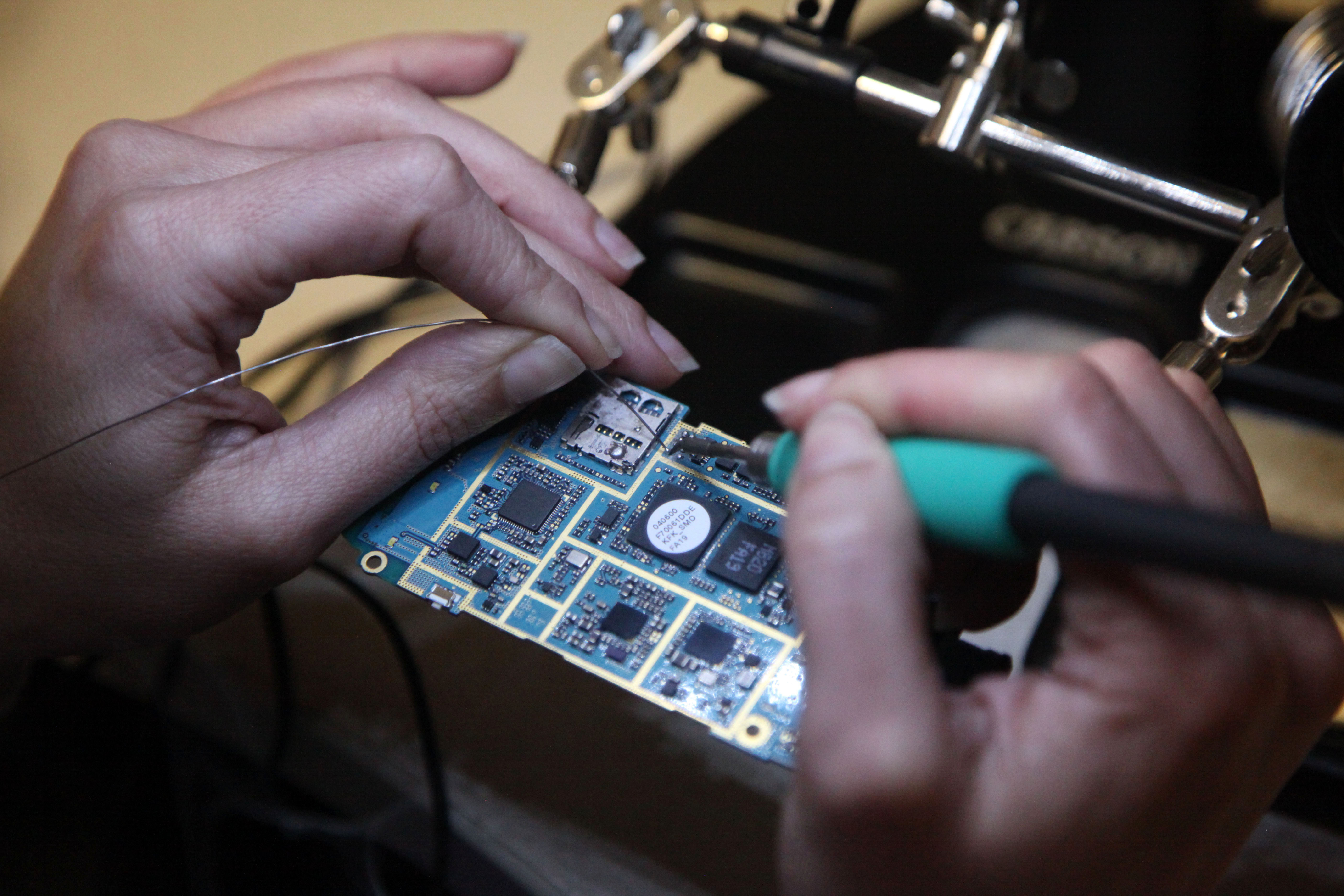 a person's hands as they use a soldering iron to attach wires to a circuit board.