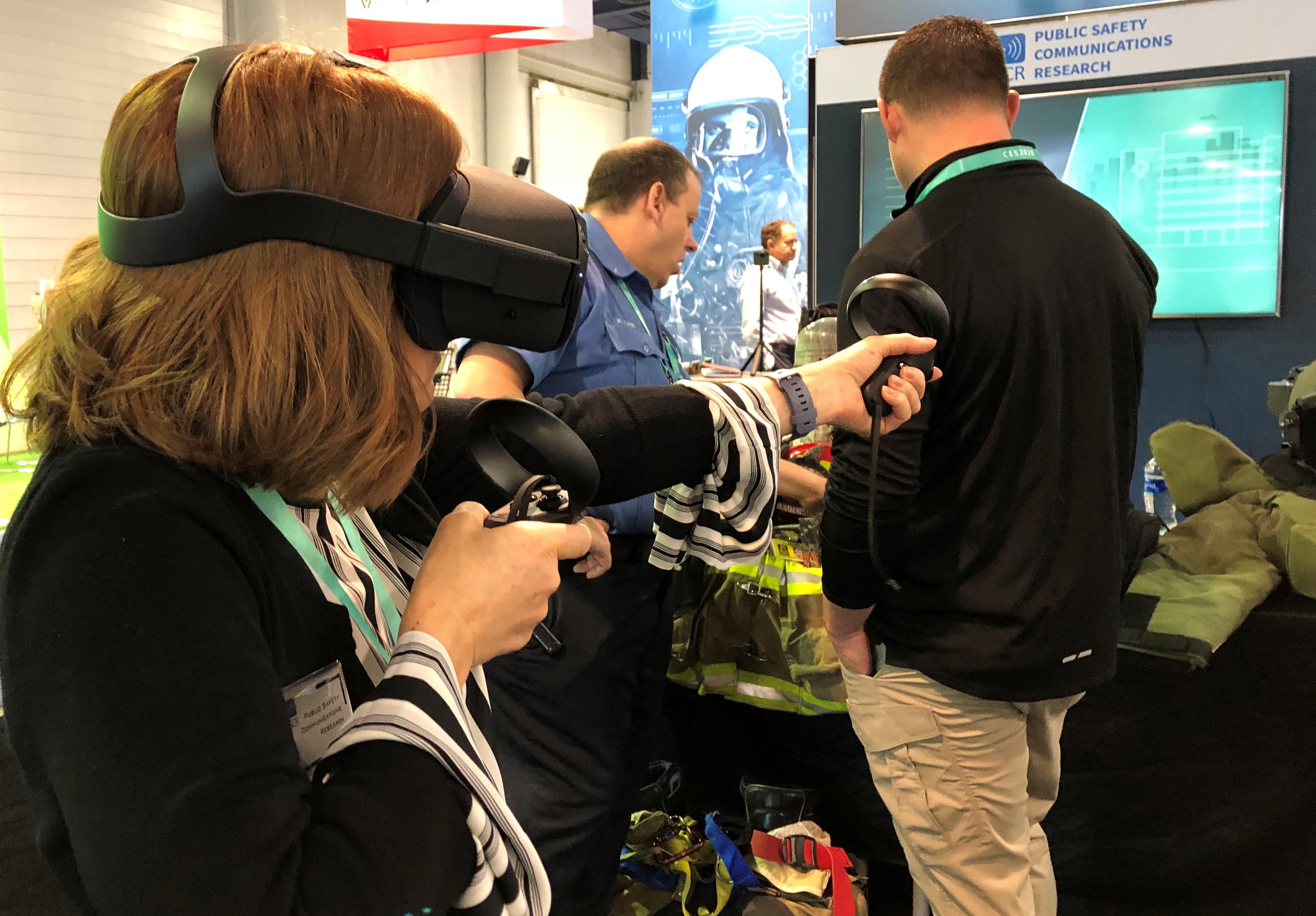 This photograph shows a woman wearing a virtual reality headset and holding controllers in her hands. She is trying out a SWAT scenario demonstration.