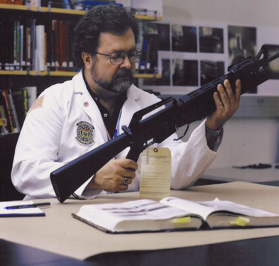 a bearded man with glasses inspecting an AR-15 assault-style weapon