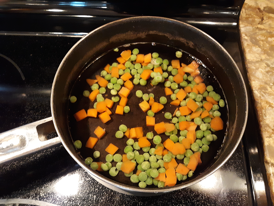 Peas and carrots in a pan filled with room temperature water. The peas and carrots are mixed and neither are floating. 
