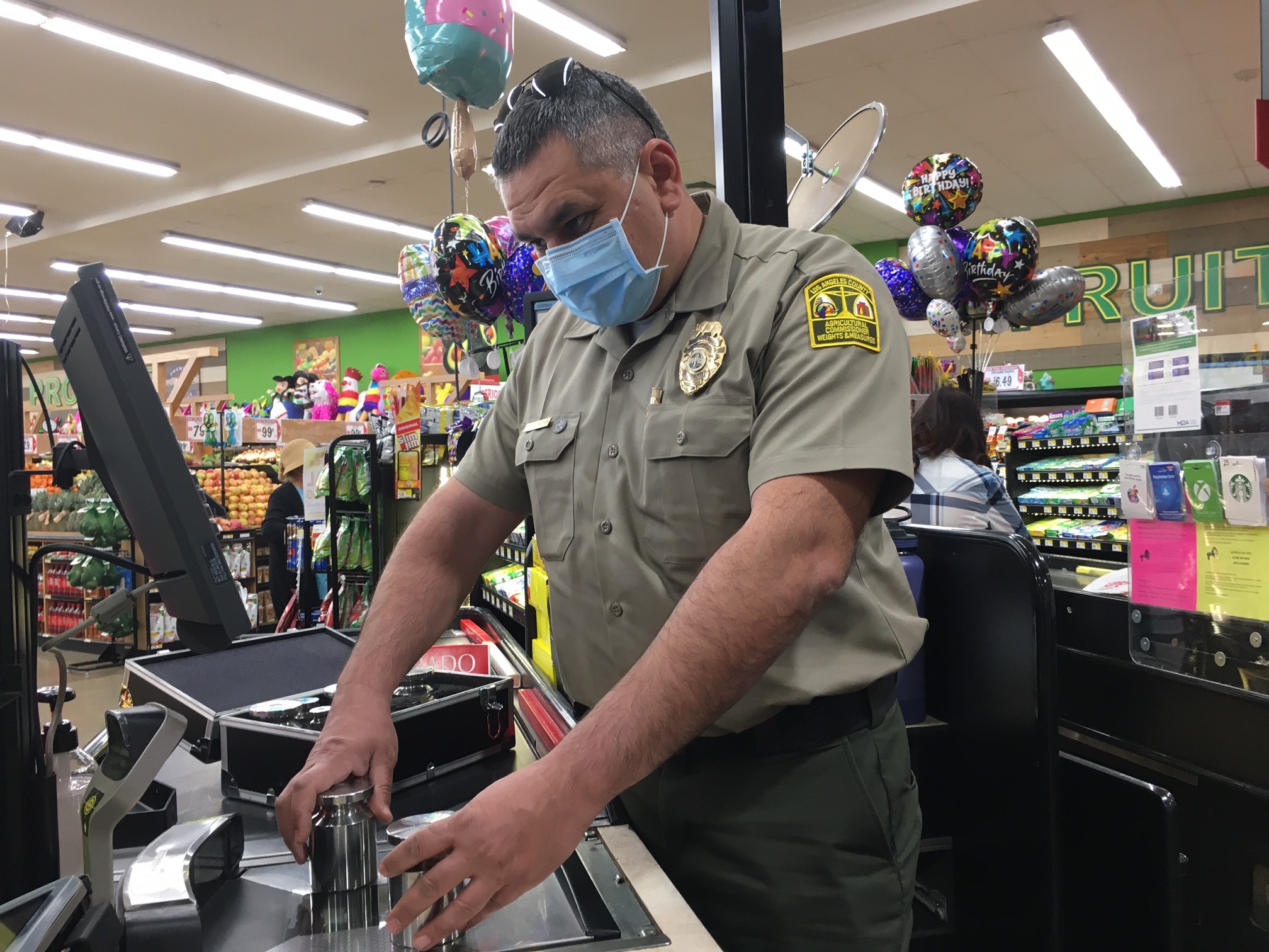 uniformed and weights and measures inspector places test measures on a grocery scale.