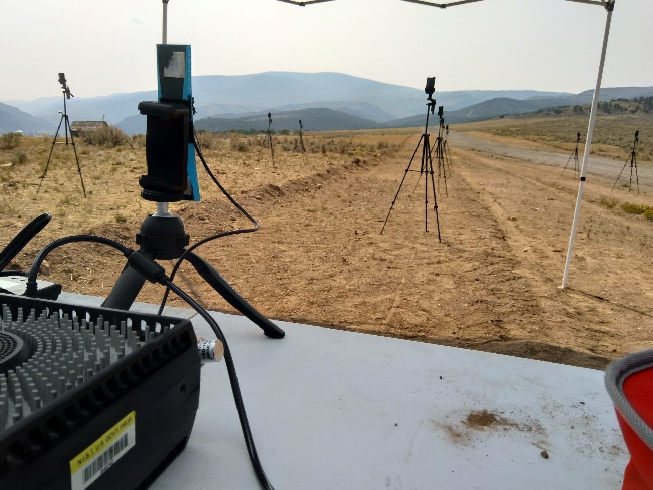 radio equipment on a table in front of cell phones mounted on tripods in a field