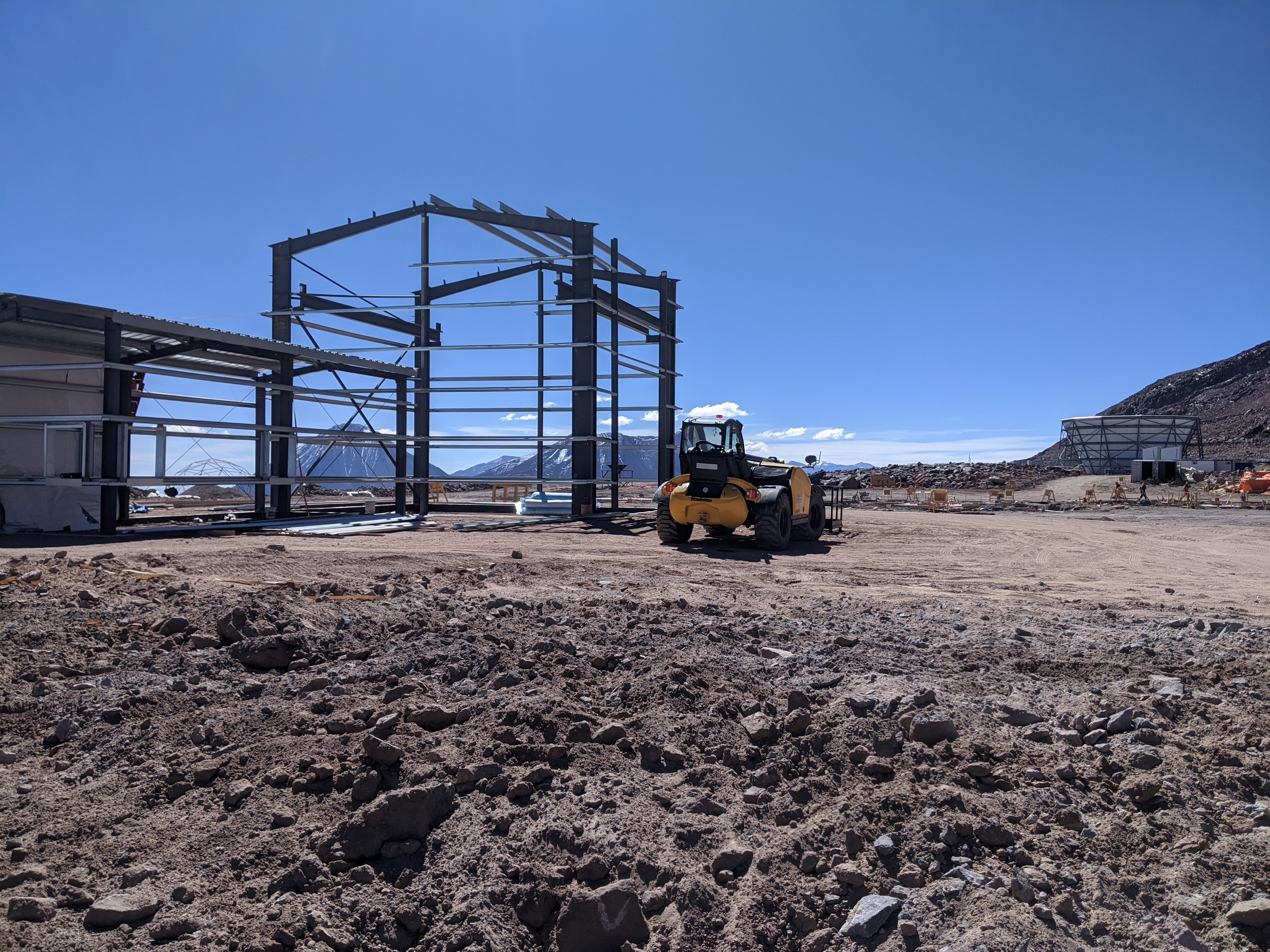 Beams of a building under construction stand in a desert under a blue sky.
