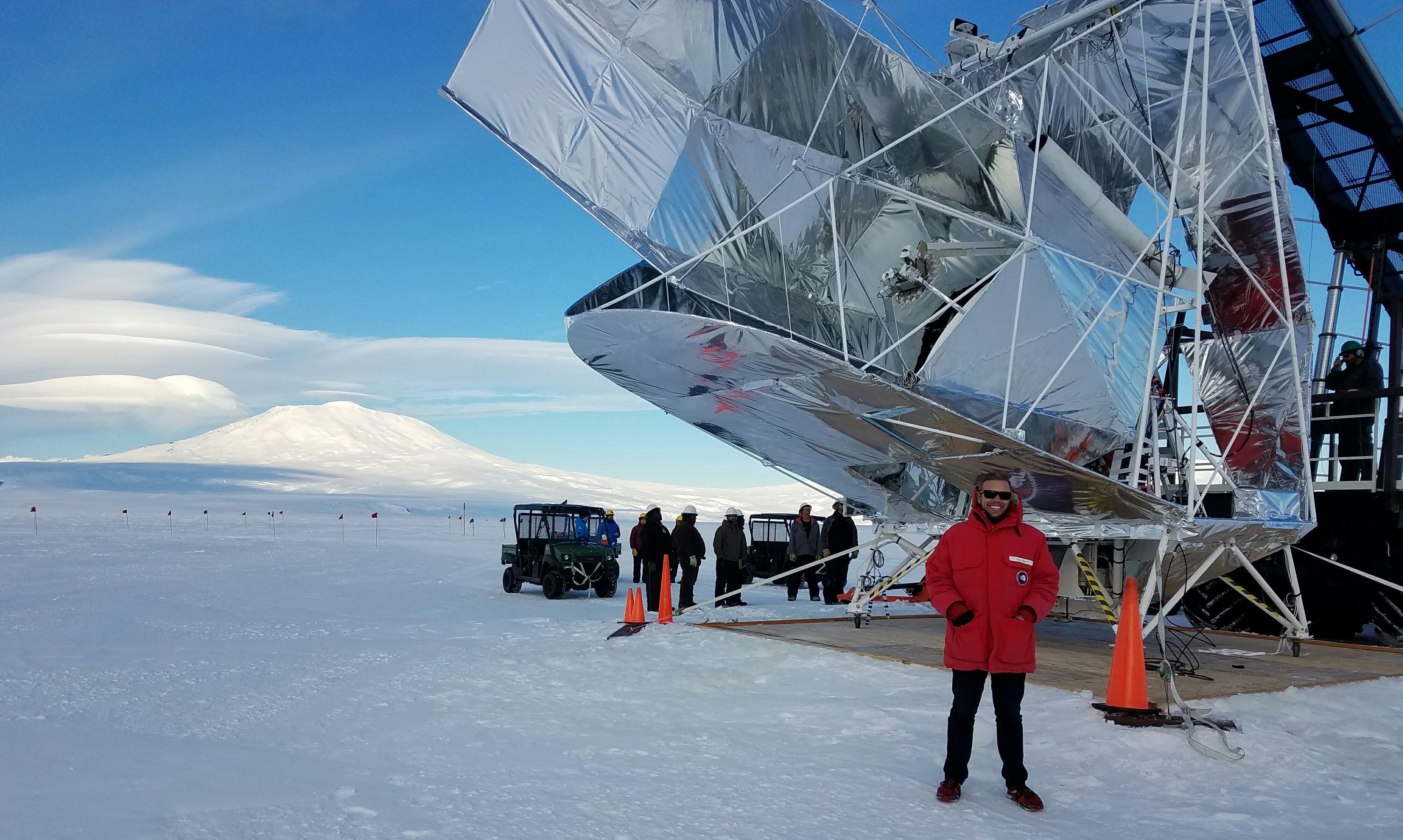 A person in a red parka stands on snow in front of a large metallic balloon structure.