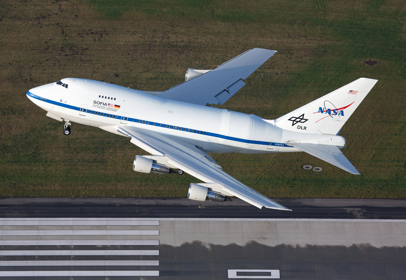 A white airplane with a NASA logo takes off from a runway. 
