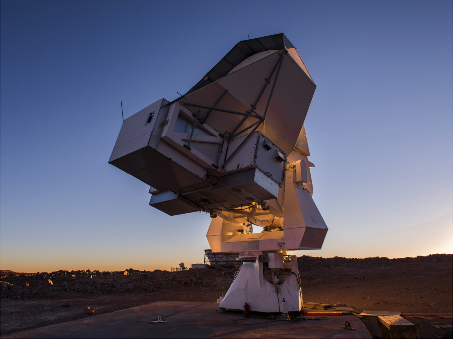 A large telescope structure rises from a rocky terrain. 