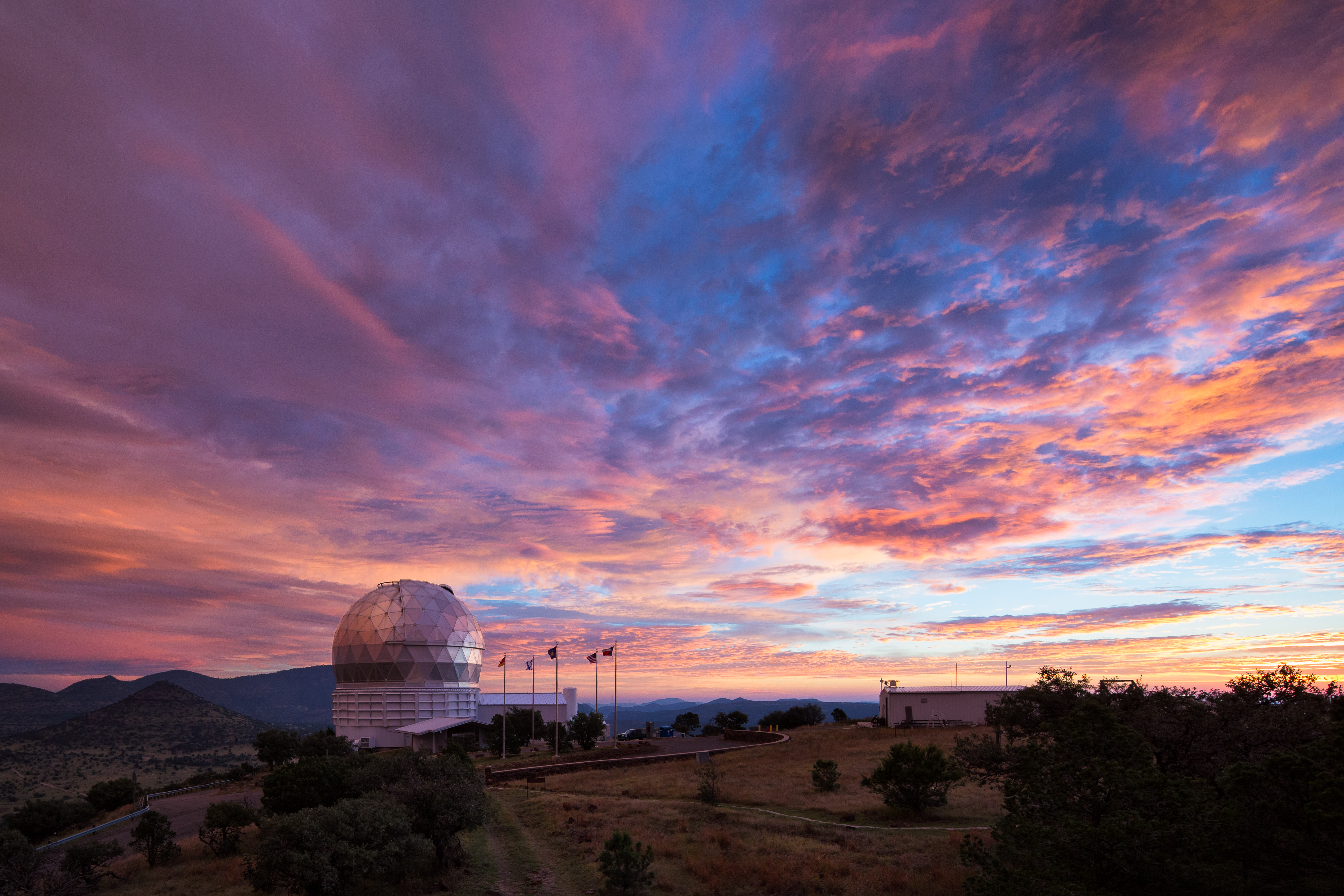 The dome of an observatory is silhouetted against a dramatically colorful sky. 