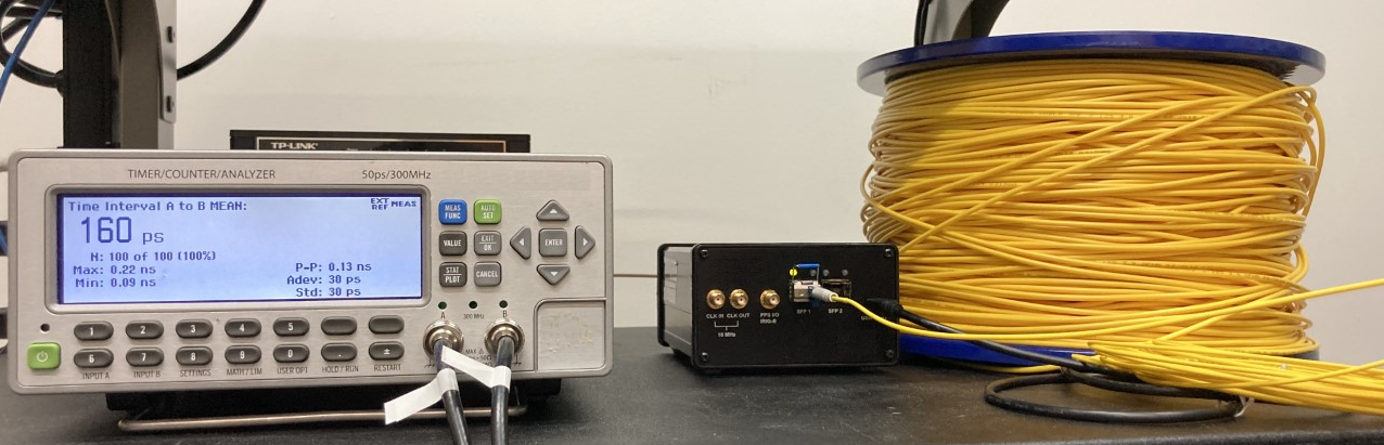 A small rectangular device with a display screen and buttons sits next to a spool of yellow fiber. 