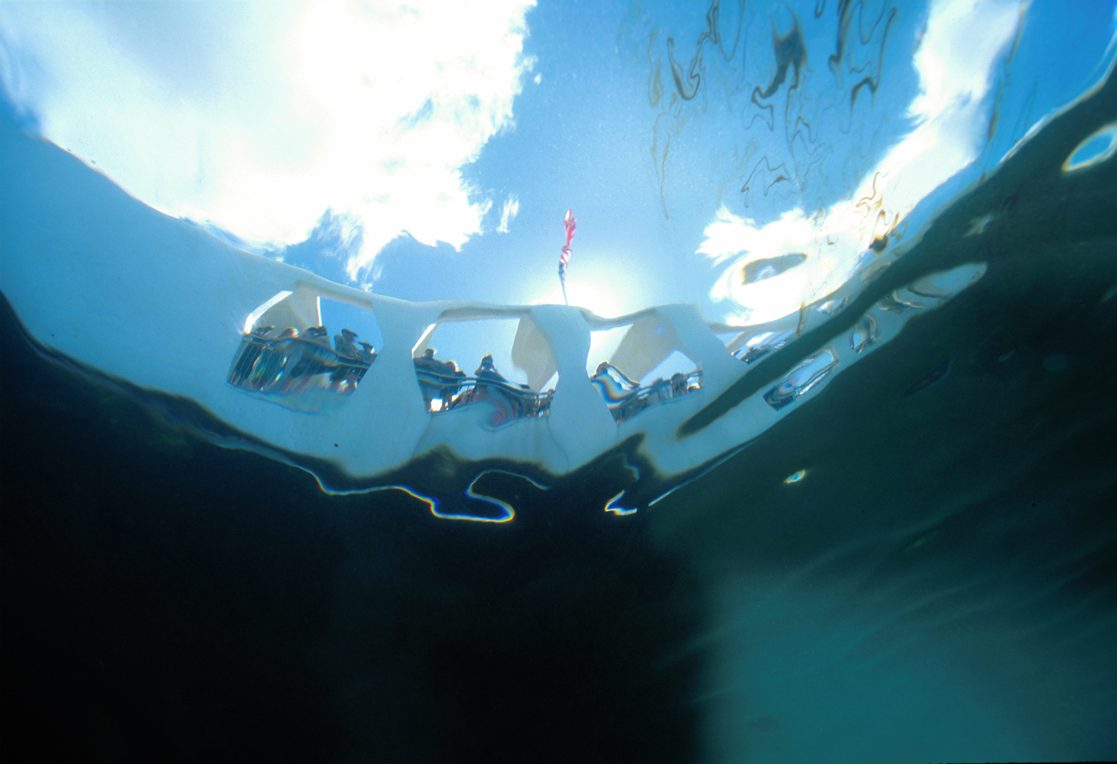 A view from underwater shows people looking over the railing at the USS Arizona memorial.