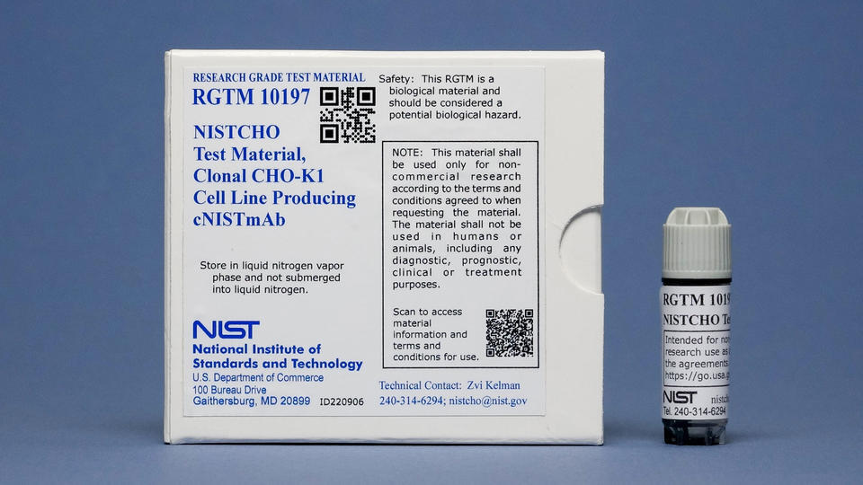 A small vial is displayed to the right of a square white box with various labels including "NISTCHO Test Material" and "NIST."