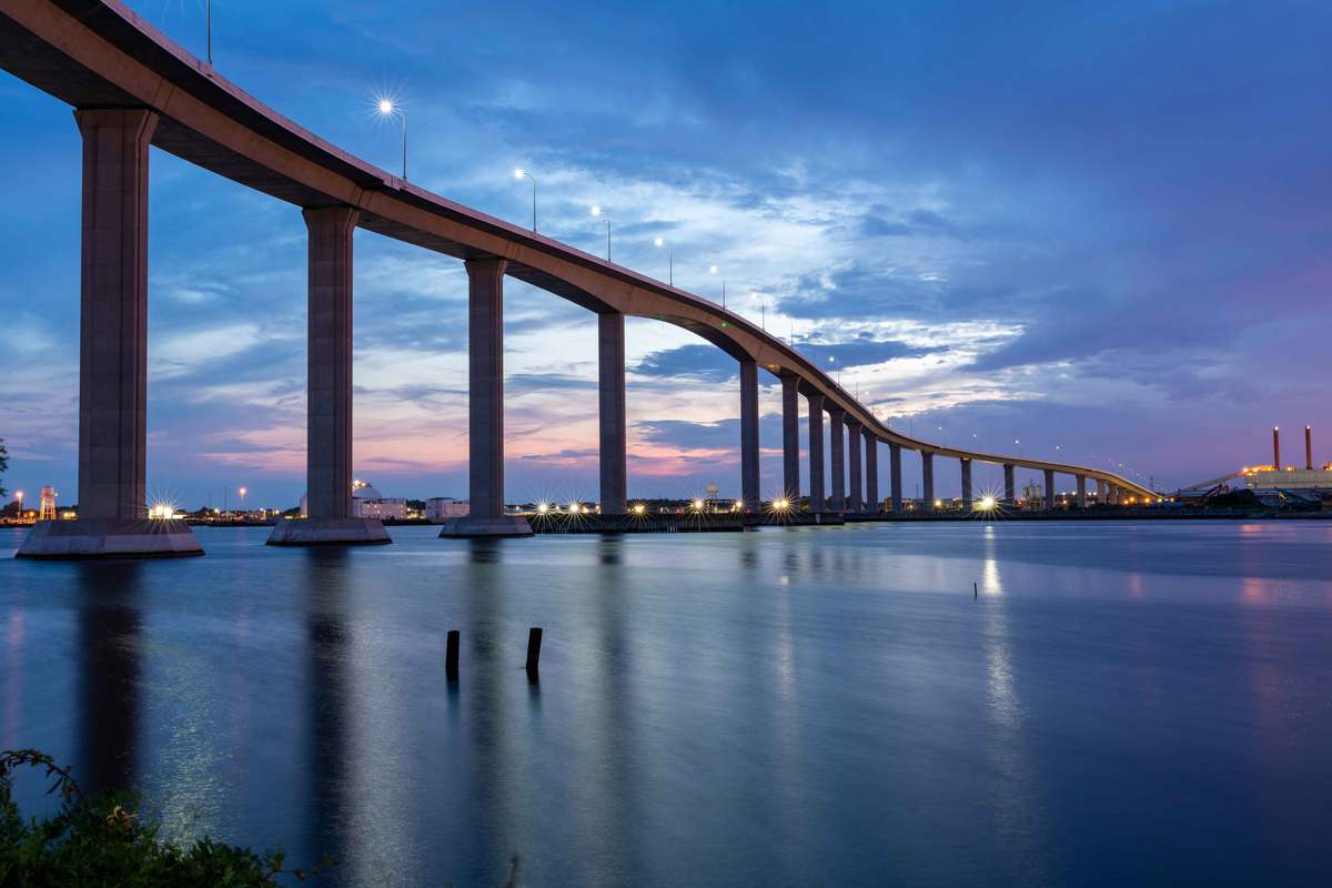 View from below of a high, long bridge on concrete supports against a darkening sky.