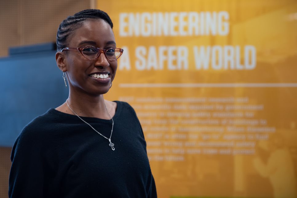 Jazalyn Dukes poses in front of a display that reads "Engineering a Safer World."