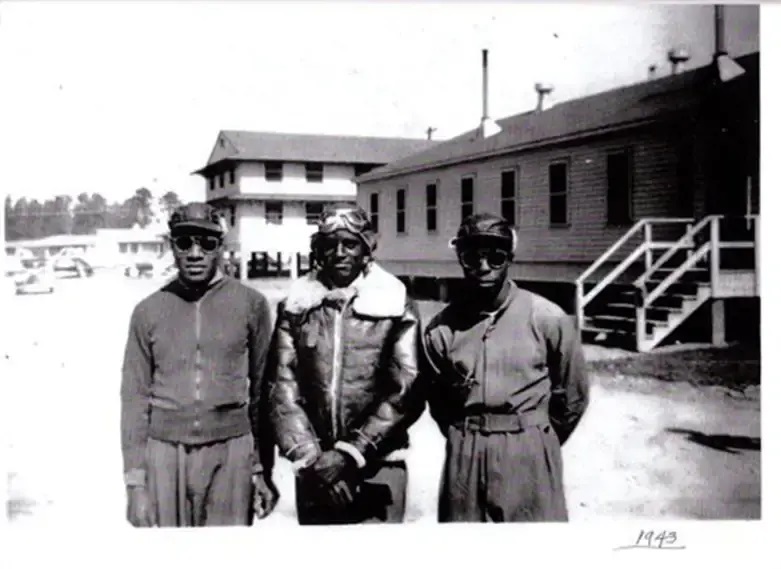 Historical photo shows three men in military aviation gear standing in front of a barracks.