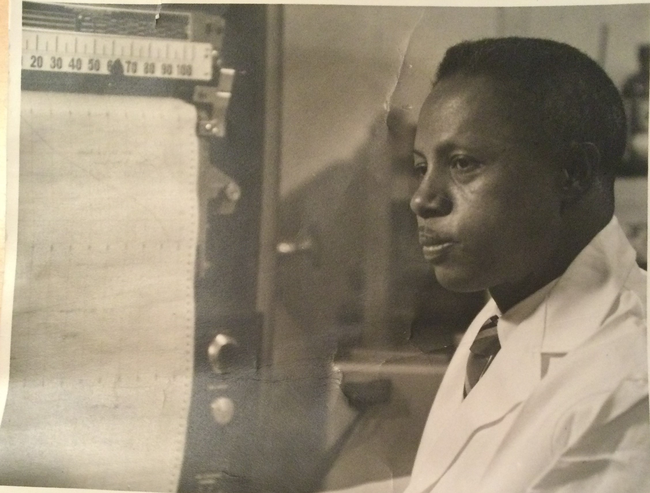 James E. Fearn stands in a white lab coat next to scientific equipment in a historical photo. 