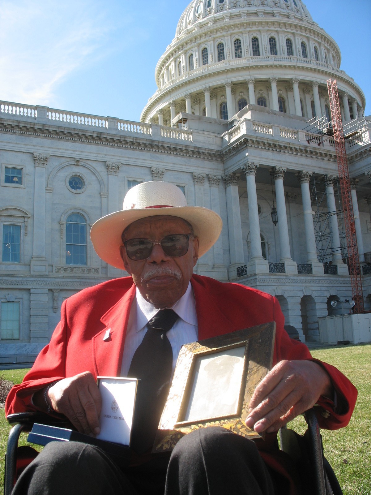 Moe Thomas Jr. poses outside the U.S. Capitol with a Congressional Gold Medal and a framed photo of himself as a young airman.
