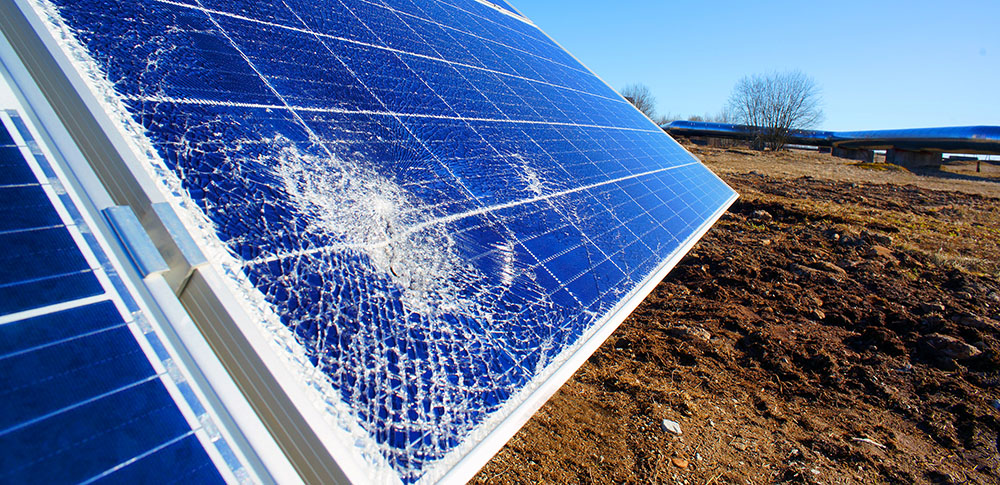 A ground-mounted solar panel has a spiderweb crack in the lower left-hand corner. 